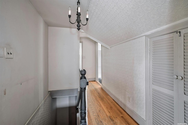 corridor with a notable chandelier, wood-type flooring, and vaulted ceiling