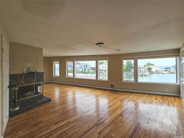 unfurnished living room with a baseboard heating unit, a water view, light hardwood / wood-style flooring, and a tiled fireplace