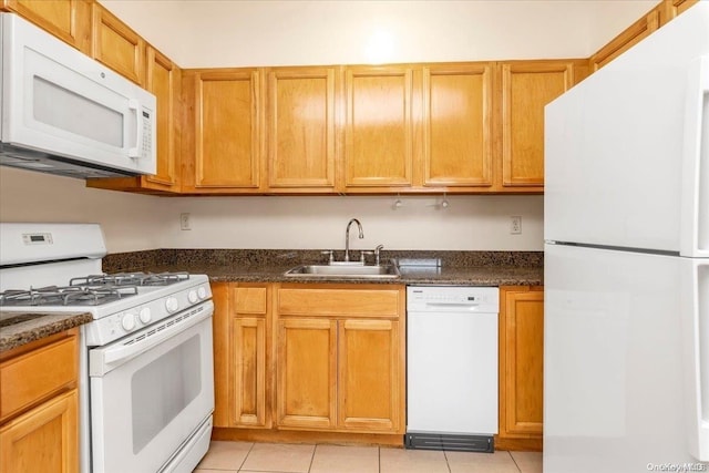 kitchen featuring light tile patterned floors, white appliances, dark stone counters, and sink