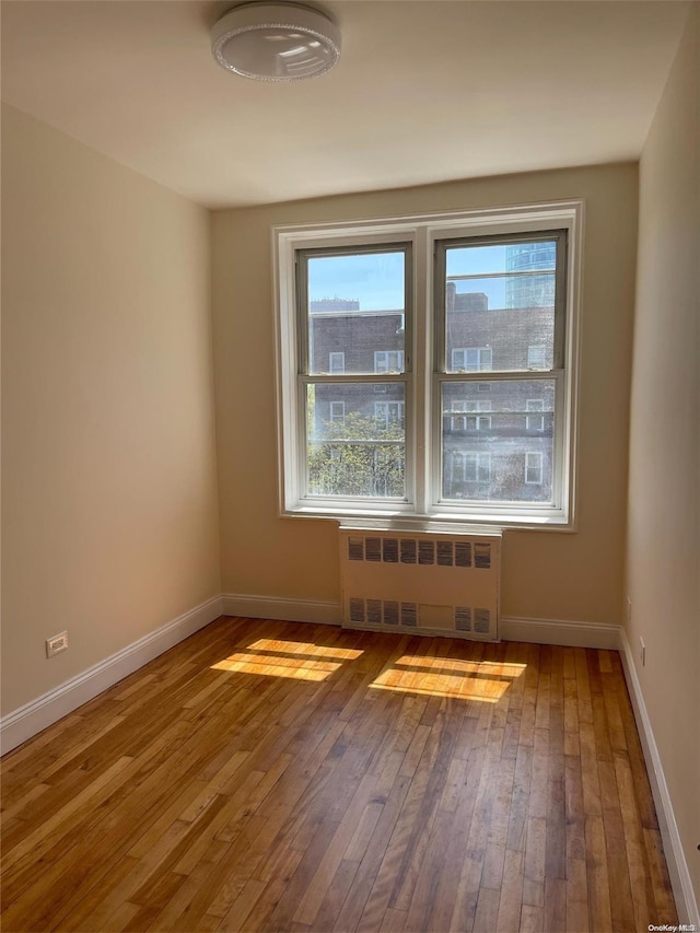 unfurnished room featuring radiator, plenty of natural light, and hardwood / wood-style flooring