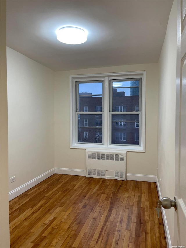 unfurnished room with radiator heating unit and hardwood / wood-style flooring