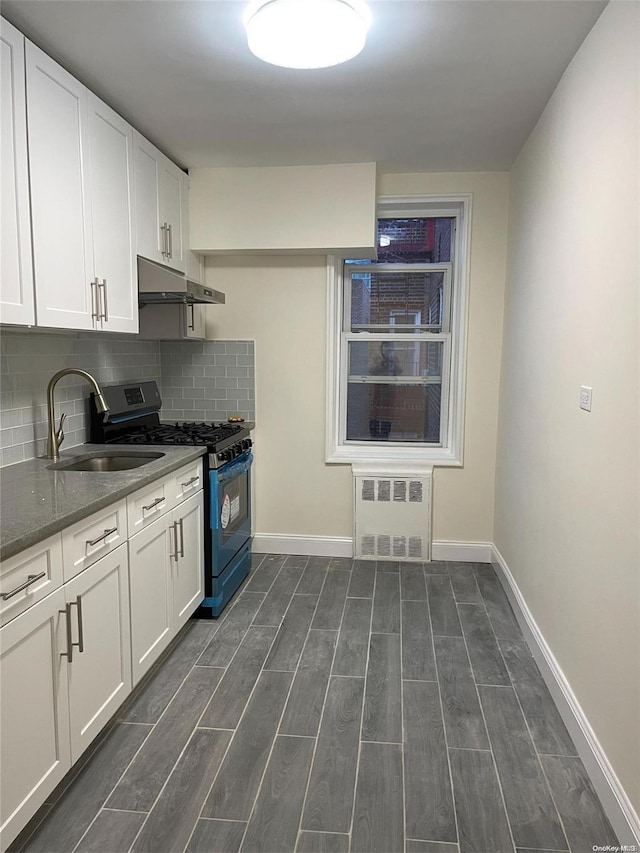 kitchen featuring dark stone counters, radiator, stainless steel gas range, dark hardwood / wood-style flooring, and white cabinetry