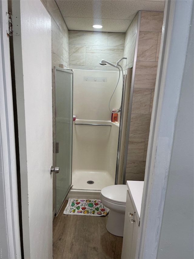 bathroom with vanity, a drop ceiling, a shower with door, hardwood / wood-style flooring, and toilet