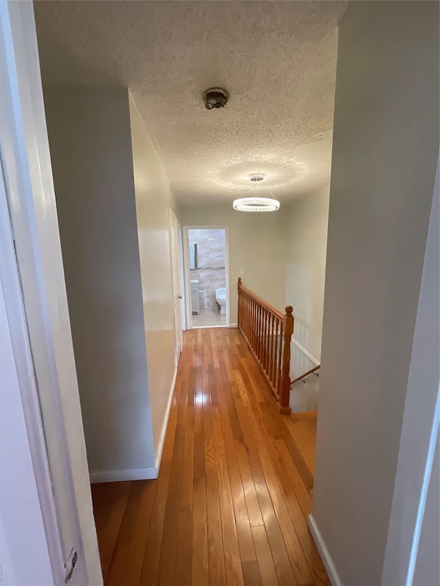 hall with a textured ceiling, hardwood / wood-style flooring, and an inviting chandelier