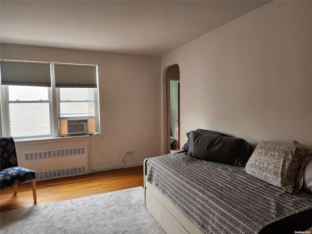 bedroom with radiator heating unit, cooling unit, and light hardwood / wood-style floors