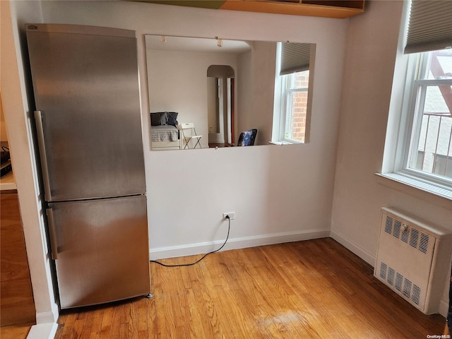 kitchen with a wealth of natural light, stainless steel fridge, radiator heating unit, and light hardwood / wood-style flooring