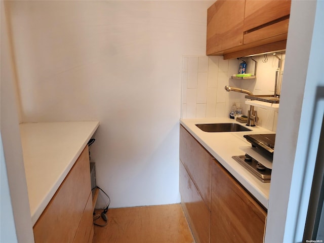 kitchen with stainless steel stovetop, tasteful backsplash, light hardwood / wood-style flooring, and sink