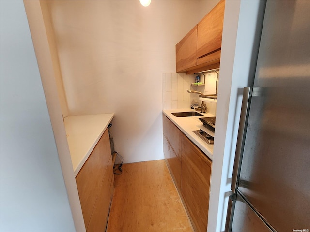 kitchen with decorative backsplash, light wood-type flooring, sink, and stainless steel refrigerator