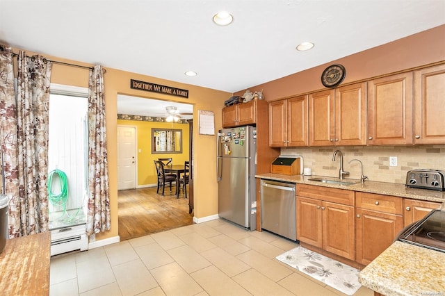 kitchen with backsplash, light stone counters, stainless steel appliances, a baseboard heating unit, and sink