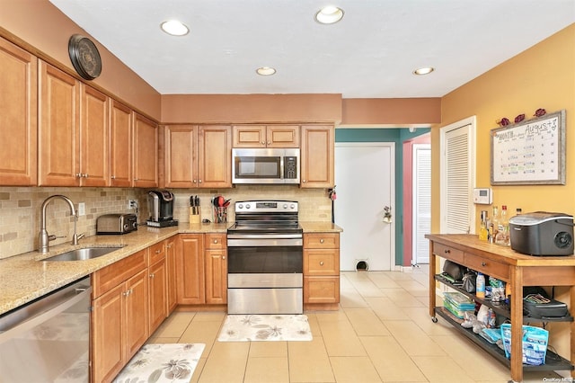 kitchen featuring backsplash, light stone counters, sink, and appliances with stainless steel finishes