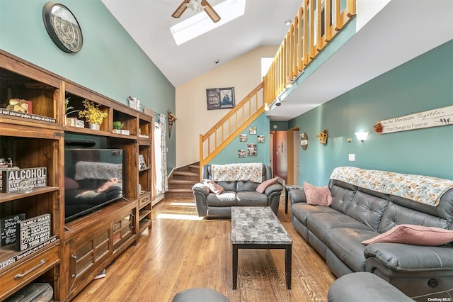 living room with a skylight, high vaulted ceiling, ceiling fan, and light hardwood / wood-style floors