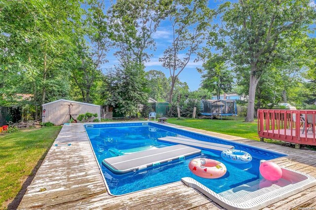 view of swimming pool featuring a trampoline, a deck, and a lawn