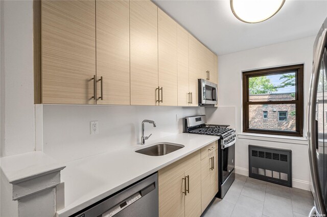 kitchen featuring light brown cabinetry, stainless steel appliances, heating unit, sink, and light tile patterned flooring