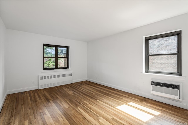 empty room featuring hardwood / wood-style floors, radiator heating unit, and a wall unit AC