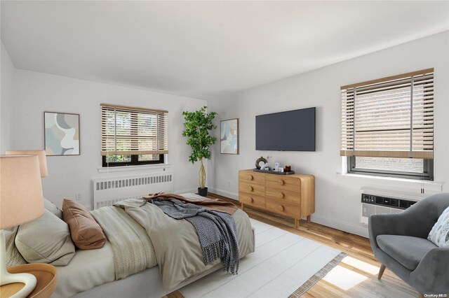 bedroom featuring a wall mounted air conditioner, light hardwood / wood-style floors, and radiator