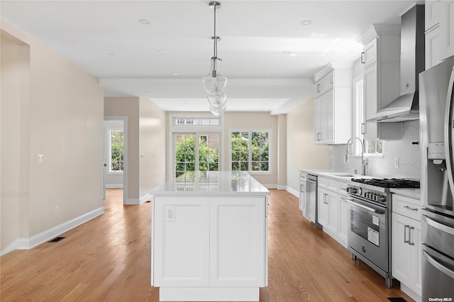 kitchen featuring appliances with stainless steel finishes, wall chimney range hood, white cabinets, a center island, and hanging light fixtures