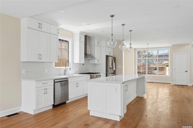 kitchen featuring appliances with stainless steel finishes, wall chimney range hood, pendant lighting, white cabinets, and a center island