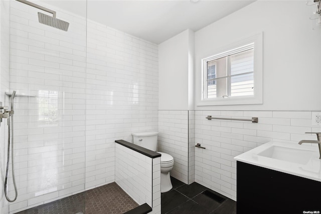 bathroom with tile patterned flooring, toilet, a tile shower, and tile walls