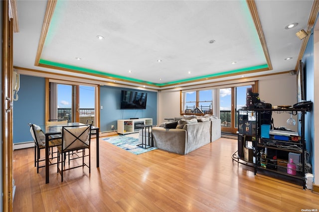 living room featuring a baseboard heating unit, light hardwood / wood-style floors, a tray ceiling, and a healthy amount of sunlight