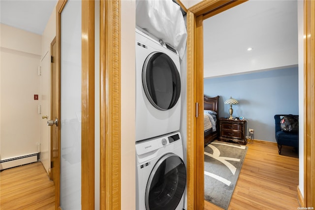 clothes washing area featuring light wood-type flooring, stacked washer and dryer, and a baseboard radiator