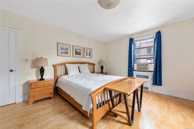 bedroom with radiator heating unit, light wood-type flooring, and cooling unit