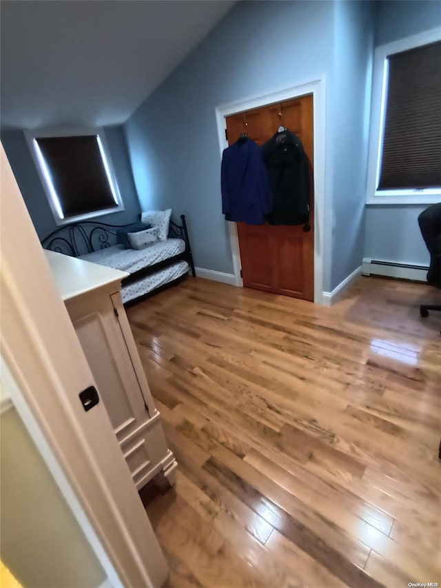 bedroom with vaulted ceiling, a baseboard heating unit, and light wood-type flooring