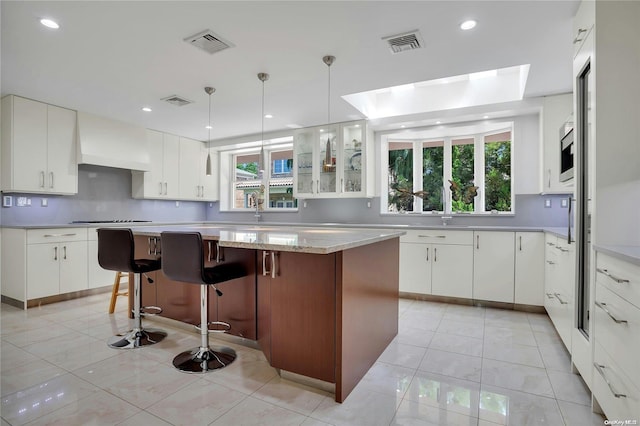 kitchen featuring a skylight, white cabinets, a breakfast bar area, a kitchen island, and custom exhaust hood