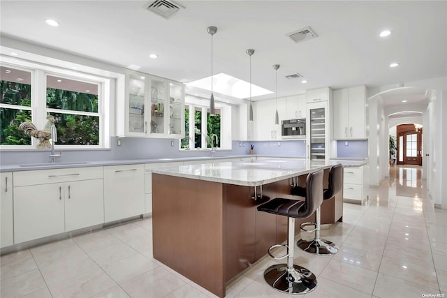 kitchen featuring a kitchen island, stainless steel microwave, white cabinetry, and a healthy amount of sunlight