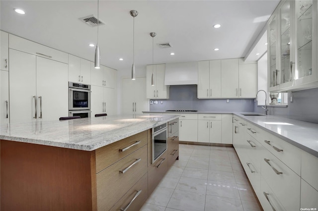 kitchen featuring white cabinetry, sink, stainless steel appliances, decorative light fixtures, and custom exhaust hood