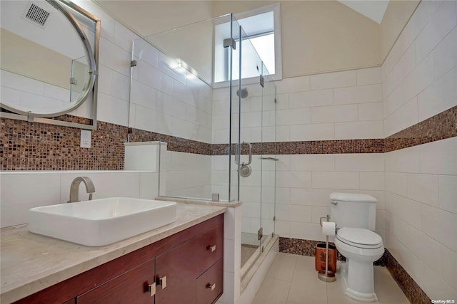 bathroom with vanity, a shower with door, tile patterned floors, toilet, and tile walls