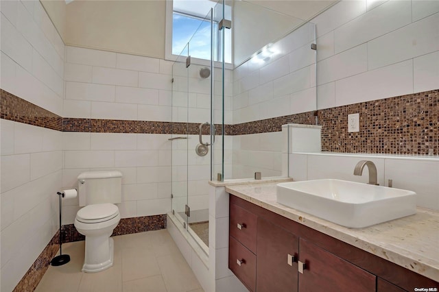 bathroom featuring vanity, a shower with door, tile patterned flooring, toilet, and tile walls