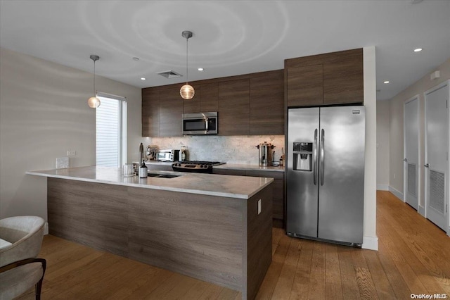 kitchen featuring sink, hanging light fixtures, light wood-type flooring, tasteful backsplash, and stainless steel appliances