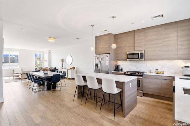 kitchen featuring appliances with stainless steel finishes, light wood-type flooring, tasteful backsplash, pendant lighting, and a kitchen island