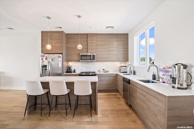 kitchen featuring sink, a center island, hanging light fixtures, light hardwood / wood-style floors, and appliances with stainless steel finishes