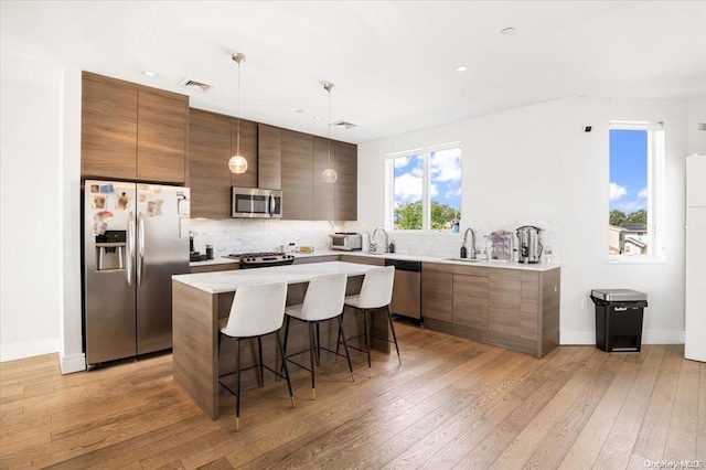 kitchen with a kitchen bar, light wood-type flooring, hanging light fixtures, and appliances with stainless steel finishes