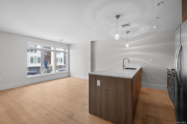 kitchen with sink, appliances with stainless steel finishes, hanging light fixtures, light stone counters, and light hardwood / wood-style floors