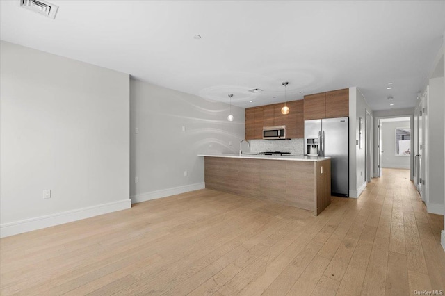 kitchen with tasteful backsplash, appliances with stainless steel finishes, hanging light fixtures, and light wood-type flooring