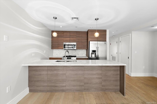 kitchen featuring stainless steel appliances, tasteful backsplash, light wood-type flooring, and decorative light fixtures