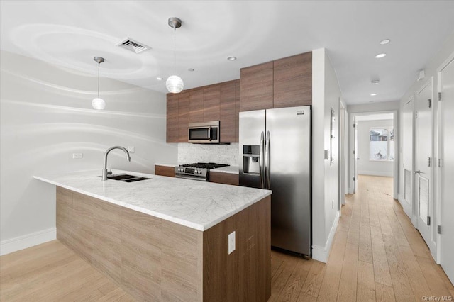 kitchen with sink, light hardwood / wood-style flooring, hanging light fixtures, stainless steel appliances, and light stone counters