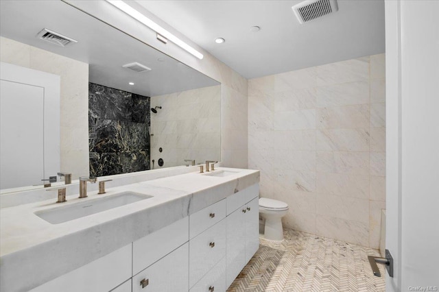 bathroom featuring tiled shower, vanity, toilet, and tile walls