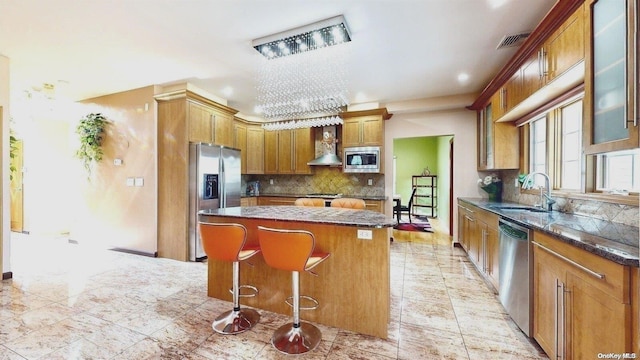 kitchen featuring a center island, wall chimney exhaust hood, stainless steel appliances, sink, and a breakfast bar area