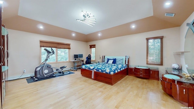 bedroom with an inviting chandelier, light hardwood / wood-style floors, a raised ceiling, and a baseboard heating unit