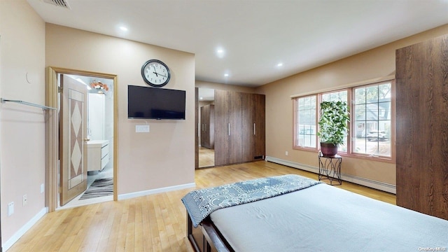 bedroom with ensuite bathroom, a baseboard radiator, and light hardwood / wood-style floors