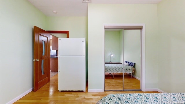 unfurnished bedroom featuring white refrigerator, light wood-type flooring, and a closet