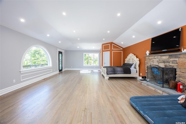 living room with vaulted ceiling, light hardwood / wood-style floors, a stone fireplace, and plenty of natural light