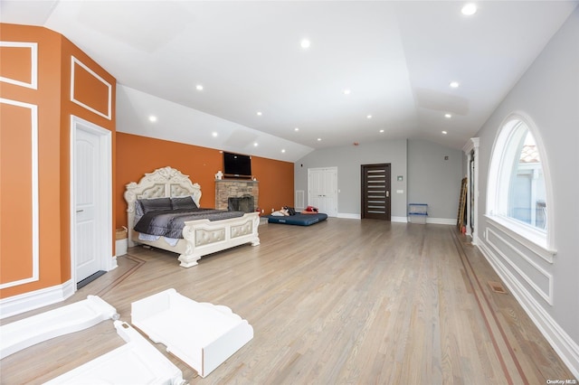 bedroom with light wood-type flooring, vaulted ceiling, and a stone fireplace