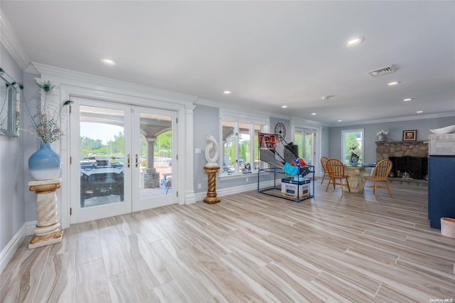 living room with a stone fireplace, french doors, light hardwood / wood-style flooring, and ornamental molding