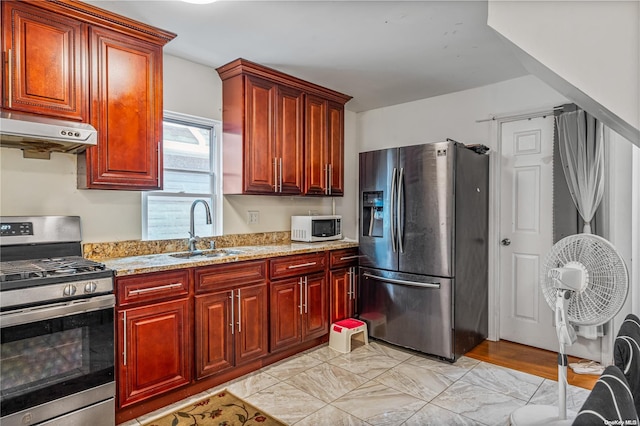 kitchen featuring light stone counters, sink, range hood, and appliances with stainless steel finishes