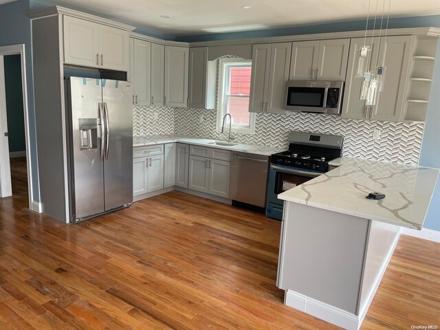 kitchen featuring hanging light fixtures, stainless steel appliances, tasteful backsplash, light hardwood / wood-style flooring, and kitchen peninsula