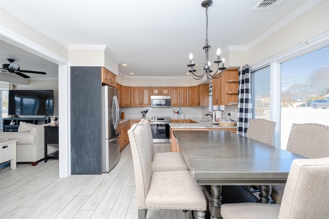 dining area with sink, crown molding, ceiling fan with notable chandelier, and light hardwood / wood-style floors